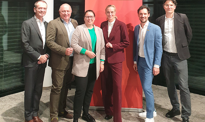 Von Klimarisiko zu Wettbewerbsvorteil: CEO Business Dinner Salzburg setzt Impulse / Alexander Fiedler Sechs Personen stehen nebeneinander vor einem roten Hintergrund, alle in formeller Kleidung. Zwei tragen Anzüge in Braun- und Blautönen, während eine Person einen auffälligen roten Anzug trägt. Die Gruppe posiert lächelnd für das Foto.