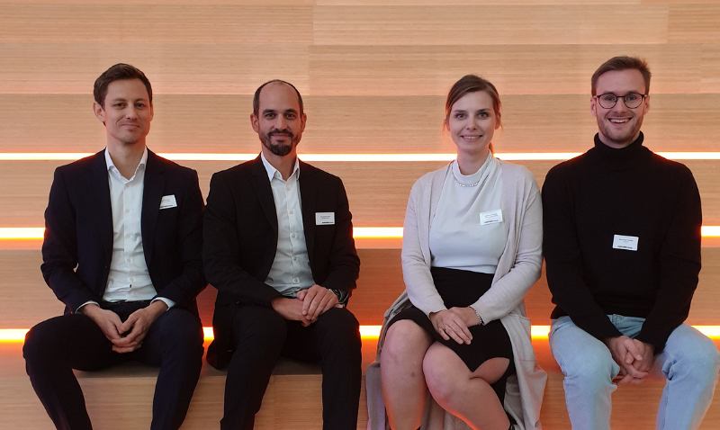 NHF Vorarlberg / respACT Vier Personen sitzen nebeneinander auf einer Treppe mit beleuchteten Stufen; zwei Männer tragen Anzüge, während die Frau und der vierte Mann in eleganter Kleidung gekleidet sind.